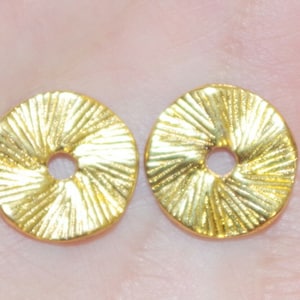 May include: Two gold-colored metal round decorative embellishments with a raised, sunburst design. The embellishments have a hole in the center.