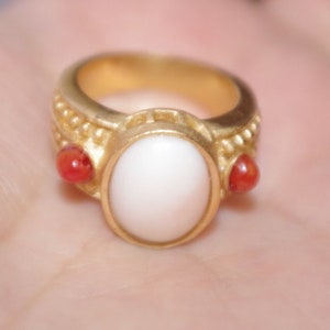 Puede incluir: Un anillo de oro con una piedra ovalada blanca y dos piedras rojas a los lados.