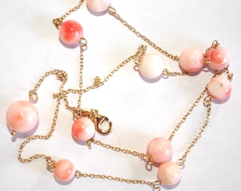 May include: A gold chain necklace with pink coral beads. The necklace has a lobster clasp closure.