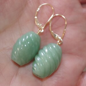May include: A pair of green jade earrings with a swirl design. The earrings are made of gold and have a leverback closure.