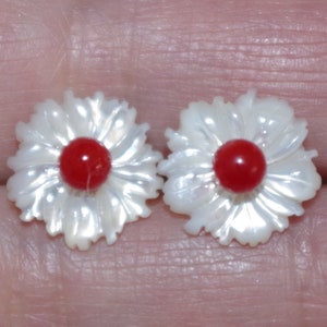 May include: Two flower-shaped earrings. Each earring features a white, iridescent petal design surrounding a vibrant red center. The earrings are small, likely for pierced ears, and have a delicate, feminine aesthetic.
