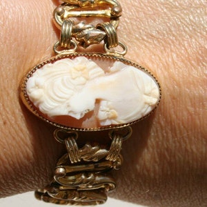Op de afbeelding: Een gouden kettingarmband met een cameo met het profiel van een vrouw. De cameo is gemaakt van schelp en is gezet in een gouden frame.