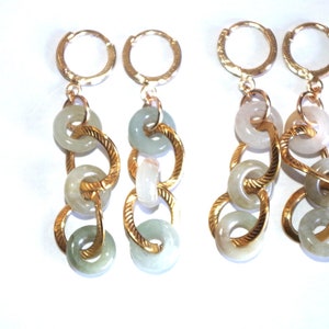 May include: A pair of gold hoop earrings with a dangling chain of jade green and white jade rings.