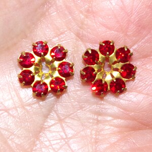 May include: Two gold-toned flower-shaped embellishments with red rhinestones.