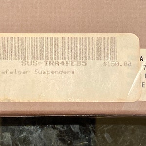 May include: A close-up of a label with a barcode and the text "Trafalgar Suspenders". The label is on a cardboard box. The label also has the text "SUS-TRA4FEB5".