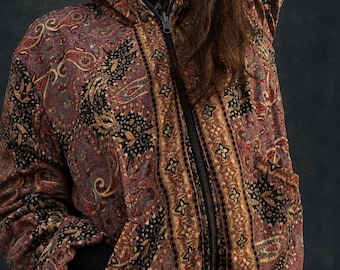 May include: A zip-up hooded jacket featuring a complex paisley pattern in shades of deep red, gold, and black. The garment includes a front zipper closure, a hood, and solid black ribbed cuffs and hem, providing a structured fit and finish.