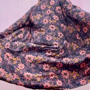 K&ouml;nnte beinhalten: Eine lange, flie&szlig;ende Robe mit Blumendruck auf dunklem Hintergrund und rosa und gelben Blumen. Die Robe ist aus weichem, seidenweichem Stoff gefertigt und hat eine lockere Passform.