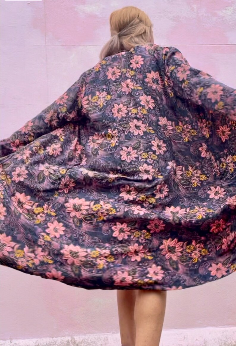 K&ouml;nnte beinhalten: Eine lange, flie&szlig;ende Robe mit Blumendruck auf dunklem Hintergrund und rosa und gelben Blumen. Die Robe ist aus weichem, seidenweichem Stoff gefertigt und hat eine lockere Passform.