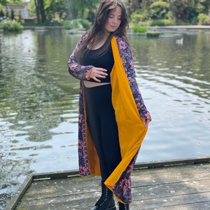 K&ouml;nnte beinhalten: Ein langer, floral gemusterter Cardigan mit gelbem Samtfutter. Der Cardigan wird &uuml;ber einem schwarzen Tanktop und schwarzen Leggings getragen. Die Person tr&auml;gt schwarze Combat Boots.
