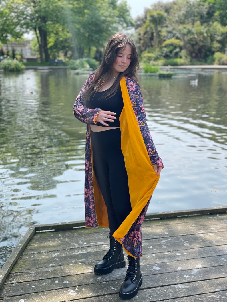 K&ouml;nnte beinhalten: Ein langer, floral gemusterter Cardigan mit gelbem Samtfutter. Der Cardigan wird &uuml;ber einem schwarzen Tanktop und schwarzen Leggings getragen. Die Person tr&auml;gt schwarze Combat Boots.