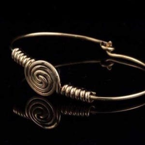Puede incluir: Un brazalete de alambre dorado con un diseño en espiral. El brazalete está abierto y tiene un cierre simple.