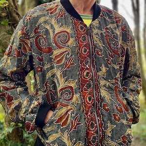 May include: A grey bomber jacket with a floral pattern in shades of red, gold, and brown. The jacket has a zip closure and a black collar.