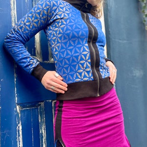 May include: A blue and gold patterned jacket with a black zipper and a fuchsia skirt with a black side panel. The skirt has a slit on the side and is worn with black fishnet tights.