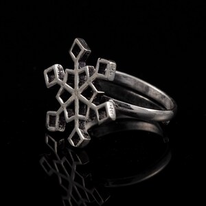 Puede incluir: Un anillo de plata con un diseño de copo de nieve. El copo de nieve es detallado e intrincado, con un patrón geométrico.