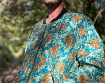 May include: A teal blue bomber jacket with a floral pattern in shades of orange, white, and green. The jacket has a zipper closure and a pocket on the left side.