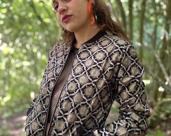 May include: A black and gold bomber jacket with a geometric pattern. The jacket has a zipper closure and two pockets.