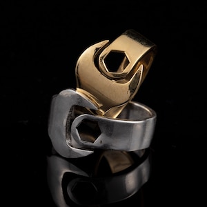 Puede incluir: Dos anillos entrelazados, uno dorado y otro plateado, con forma de llaves.