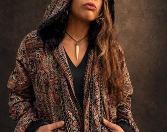 May include: A zip-up hooded jacket featuring a detailed multi-colored paisley pattern in shades of red, blue, and black. The jacket includes a black faux fur lining inside the hood, long sleeves with black cuffs, and two front pockets.