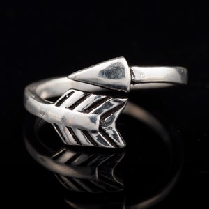 Puede incluir: Un anillo de plata con un diseño de flecha. La flecha está envuelta alrededor de la banda del anillo.