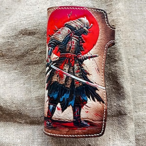 Könnte beinhalten: Ledergeldbörse mit einer detaillierten Illustration eines Samurai-Kriegers mit einem Katana-Schwert vor einem roten Sonnenhintergrund. Die Geldbörse hat eine braune Lederoberfläche mit aufwendigen Kunstwerken und Nähten.