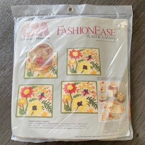 May include: A package of FashionEase plastic canvas for Floral Garden Coasters. The package shows four completed coasters with yellow and red flowers. The coasters are 4 x 4 inches. The package also shows a glass with a drink on top of a coaster.