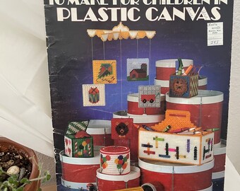 May include: A vintage craft book cover featuring colorful plastic canvas projects for children. The cover shows a variety of projects, including a mobile, pencil holder, and a box. The title of the book is "Projects to Make for Children in Plastic Canvas".