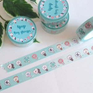 May include: Two rolls of turquoise washi tape with light blue and white designs. One roll features the text "Kpop Boy Groups" and the other roll features the text "Kpop Boy Groups" in a circle. The washi tape is on a white surface.