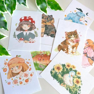 Può includere: Una collezione di stampe artistiche ad acquerello con illustrazioni fantasiose. Le stampe presentano vari soggetti, tra cui una ragazza con un cappello a fungo, un gatto con una sciarpa, un cervo, un gattino con un fiocco, una ragazza con ali di farfalla, una ragazza con un basco arancione, una ragazza con i capelli blu e un'anatra tra i girasoli.