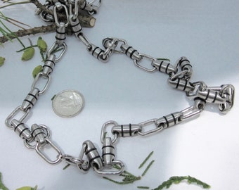 May include: A silver chain necklace with black accents. The chain is made of linked oval shapes with a small cylinder in between each link. The cylinder has a black band around the middle.