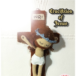 May include: A crocheted amigurumi figure of Jesus on a cross. The figure has brown hair, a crown of thorns, and is wearing a white loincloth. The cross is brown and has the inscription "INRI" on the top. The title "Crucifixion of Jesus" is written in gold lettering above the cross.