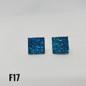 May include: A pair of square-shaped earrings with a blue glitter finish. The earrings have a silver metal setting.