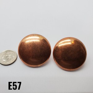 May include: A pair of large, round, copper-colored earrings. The earrings are smooth and have a shiny finish.