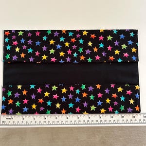 May include: A black fabric book cover with a colorful star pattern. The stars are in shades of pink, yellow, green, blue, and orange. The cover has a black band across the middle and measures approximately 13 inches wide.