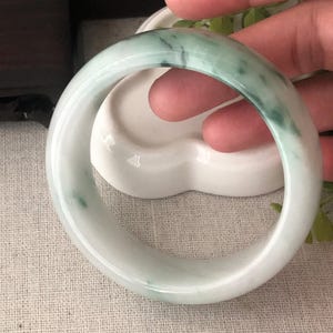 May include: A white jade bangle with green swirls. The bangle is smooth and polished.