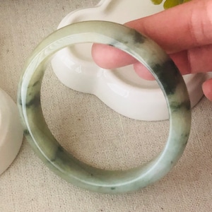 May include: A green jade bangle bracelet with a smooth, polished finish. The bracelet is a simple, elegant design.