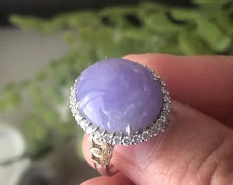 May include: A lavender jade ring with a carved design, set in a silver band with a halo of diamonds.