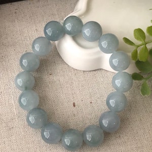 May include: A light blue jade bracelet with round beads. The bracelet is on a white surface.