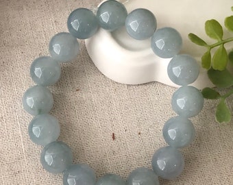 May include: A light blue jade bracelet with round beads. The bracelet is on a white surface.