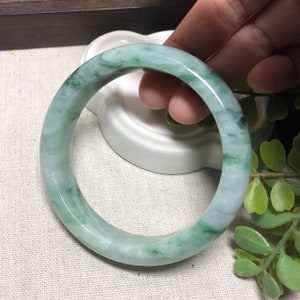 May include: A green jade bangle bracelet with a white background. The bangle is smooth and polished, with a light green colour.