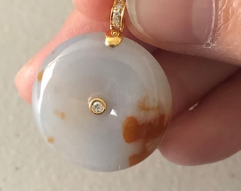 Puede incluir: Un colgante de jade gris claro con marcas marrones y un solo diamante en el centro. El colgante está unido a una cadena de oro con una fila de diamantes.