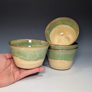 May include: Set of four ceramic bowls with a green and yellow glaze. The bowls are stacked on top of each other.