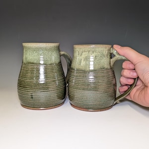 May include: A white ceramic mug with a black handle and the text "But First, Coffee" in a bold, black font. The mug is set against a neutral background, highlighting its simple design.
