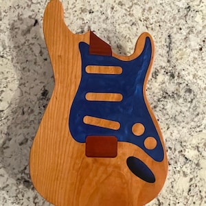 May include: Unfinished wooden guitar body with a blue and red paint design. The body is made of wood and has a natural finish.