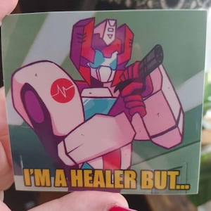 May include: A pink and red cartoon robot with a medical symbol on its arm holds a gun and says "I'm a healer but..."