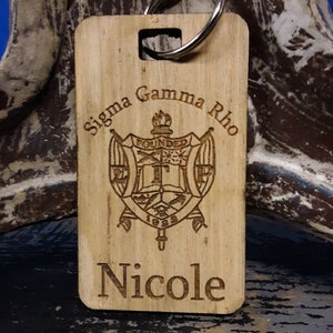 May include: A wooden keychain with a Sigma Gamma Rho sorority crest and the name "Nicole" engraved on it.