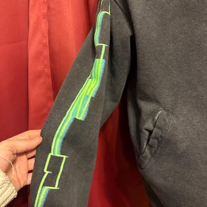 May include: Black sweatshirt with a green and blue graphic design on the sleeve. The design features geometric shapes and lines.