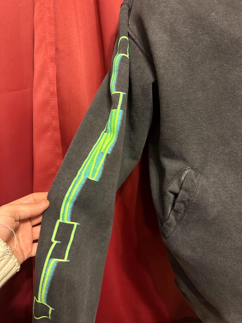 May include: Black sweatshirt with a green and blue graphic design on the sleeve. The design features geometric shapes and lines.