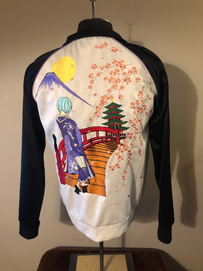 May include: Black satin bomber jacket with a white satin back panel featuring an embroidered scene of a woman in a kimono walking across a red bridge with a pagoda and cherry blossoms in the background.