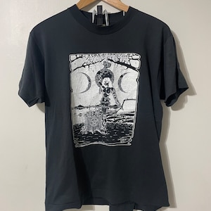 May include: Black t-shirt with a white graphic print of a witch standing in front of a crescent moon with the word "WITCH" above her.
