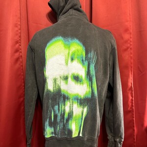 May include: Black hooded sweatshirt with a green and white graphic print of a skull on the back.
